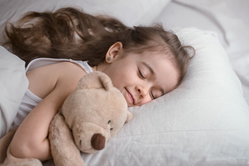 Niña durmiendo con oso en la cama después de escuchar salmos para dormir